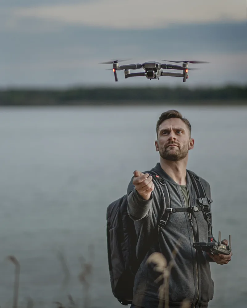 Adam nad wodą, z kontrolerem i unoszącym się przed nim dronem
